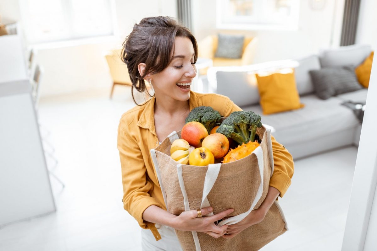 Woman with shopping bag full of fresh food indoors